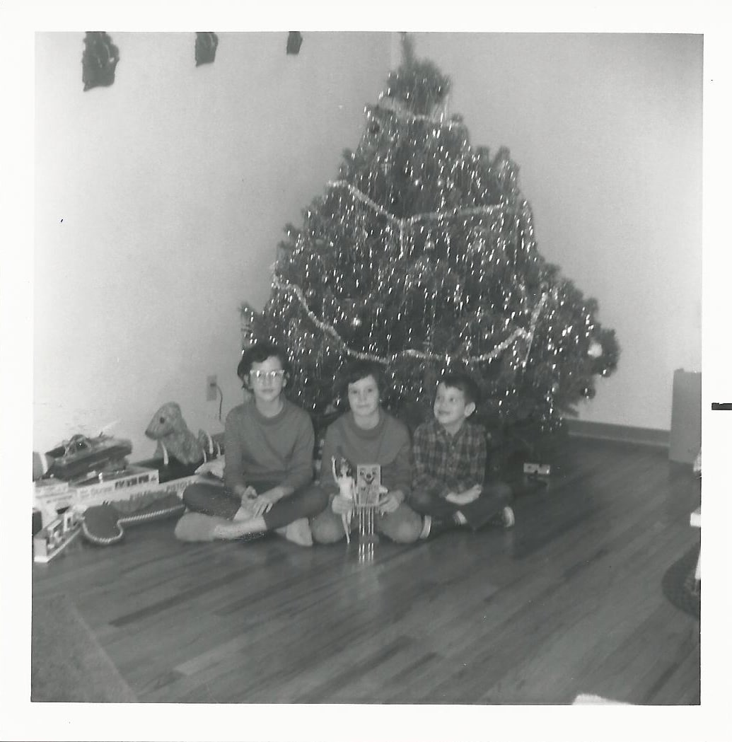 Black & white picture of 3 kids at Christmas tree in 1965